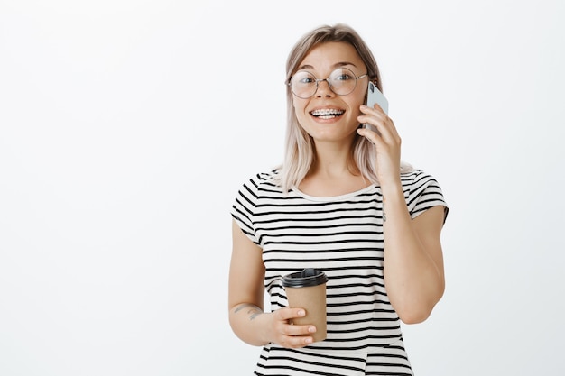 Portrait of good-looking blonde girl posing in the studio with her phone and coffee