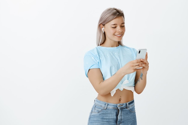 Portrait of good-looking blonde girl posing in the studio with her phone and earphones