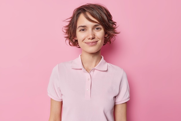 Free photo portrait of good looking brunette woman smiles tenderly has charming look wears casual t shirt looks satisfied at camera isolated over pink studioo background receives pleasant news from interlocutor