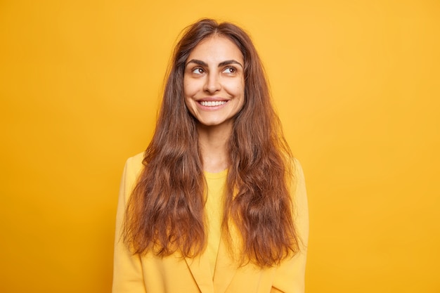 Portrait of good looking brunette young woman smiles gently has dreamy expression thinks about 