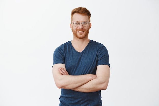 Portrait of good-looking confident redhead mature guy with bristle in round glasses, holding hands on chest and smiling broadly