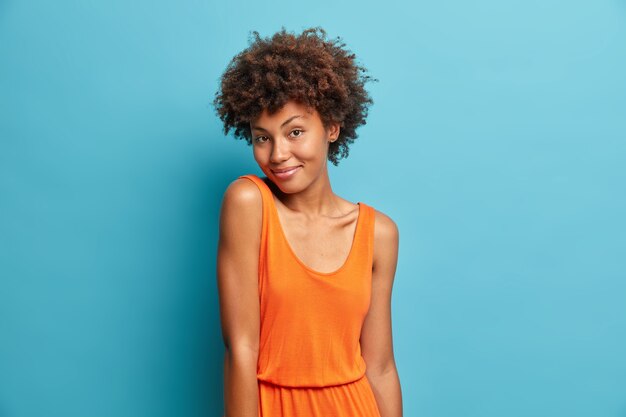 Portrait of good looking curly haired woman looks with satisfied expression