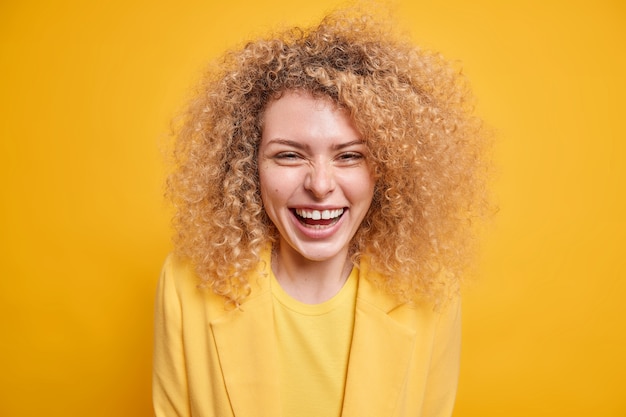 잘 생긴 곱슬머리 젊은 여성의 미소는 최근 소식을 듣고 기쁘게 긍정적인 감정을 광범위하게 표현합니다.