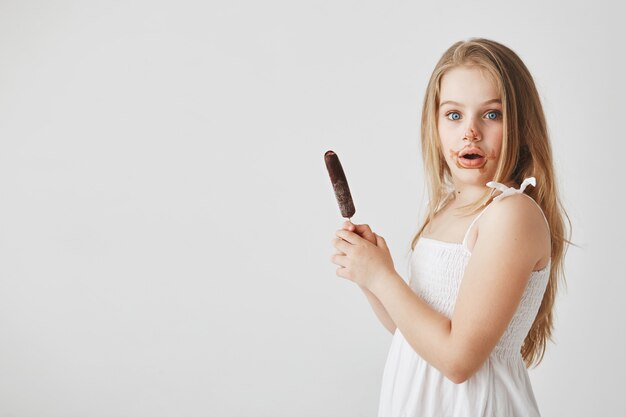 Портрет красивой смешной маленькой девочки с длинными светлыми волосами с удивленным выражением лица, будучи грязным после еды мороженого.