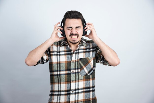 Ritratto di buon ragazzo in cuffia ascoltando la canzone sul muro bianco.