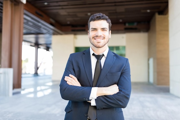 Free photo portrait of good looking hispanic businessman standing arms crossed outside office