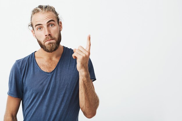 Portrait of good-looking manly guy with trendy hairstyle and beard pointing up