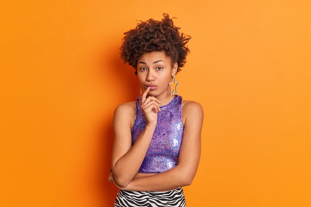 Portrait of good looking serious African American woman looks directly at camera keeps finger on lips