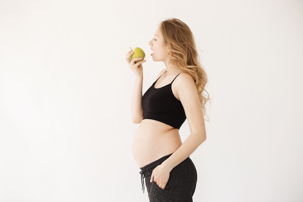 Portrait of good-looking young pregnant mother with blond hair in home wear with open stomach