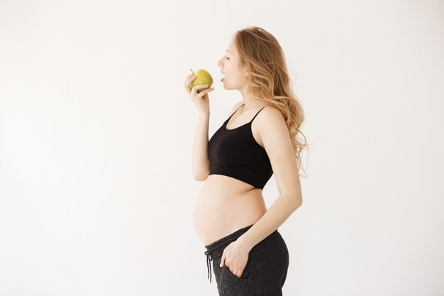 Портрет красивой молодой беременной матери со светлыми волосами в домашней одежде с открытым животом