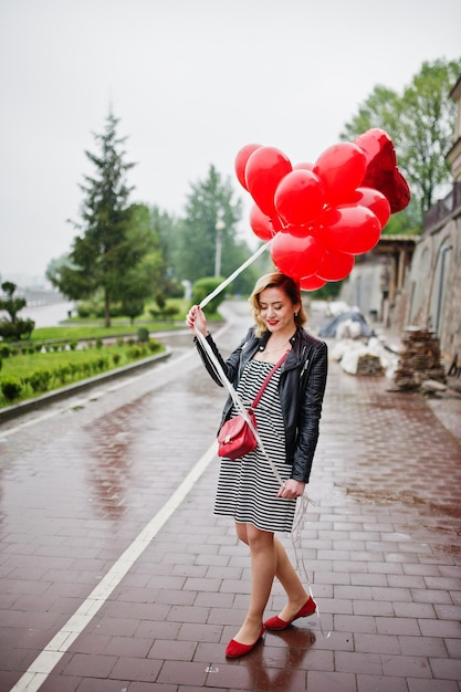 Free photo portrait of a gorgeous beautiful bridesmaid in a pretty dress holding heartshaped red balloons in the park at bachelorette party