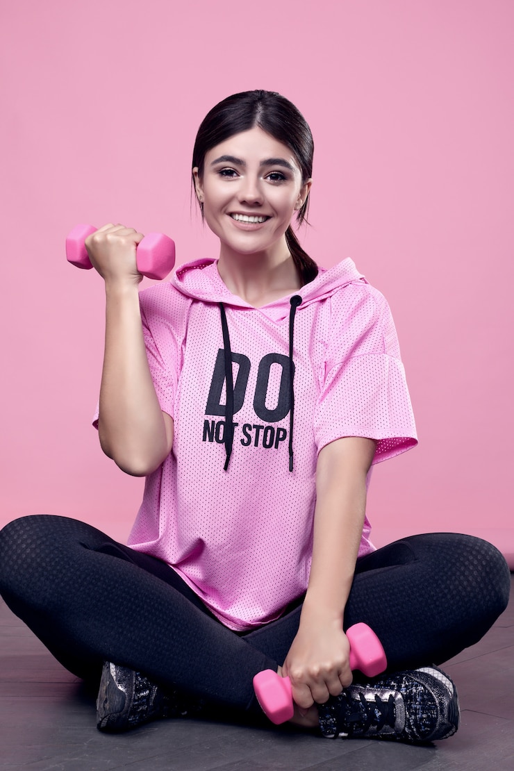 Free Photo portrait of a gorgeous body positive latin woman in a pink sports hoodie exercising with dumbbells on pink