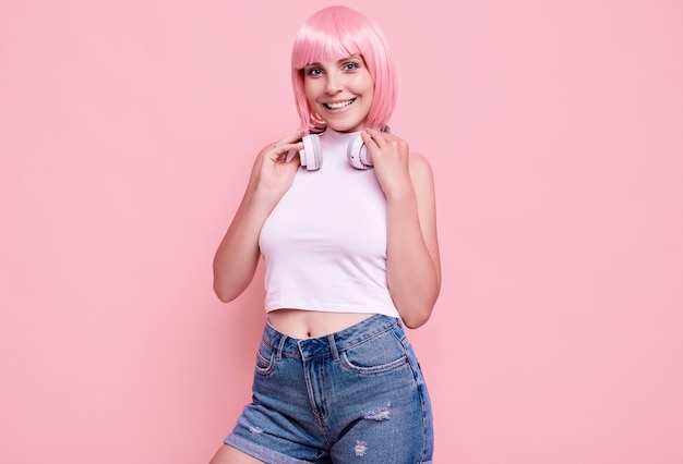 분홍색 머리를 가진 화려한 밝은 힙 스터 소녀의 초상화는 다채로운 헤드폰에서 음악을 즐깁니다.