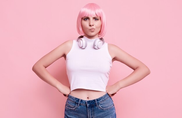 ピンクの髪のゴージャスな明るいヒップスターの女の子の肖像画は、カラフルなヘッドフォンで音楽を楽しんでいます