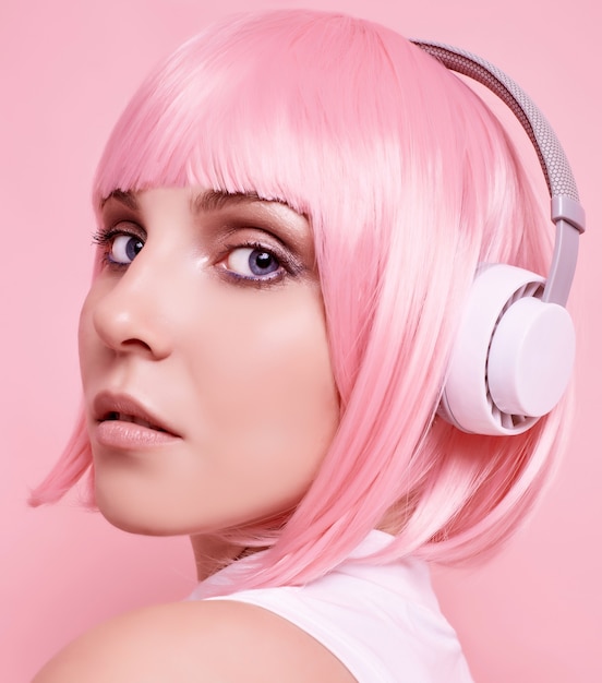 분홍색 머리를 가진 화려한 밝은 힙 스터 소녀의 초상화는 다채로운 헤드폰에서 음악을 즐깁니다.