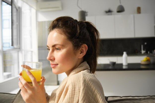 Portrait of gorgeous modern young woman wakes up in morning has her fresh glass of orange juice