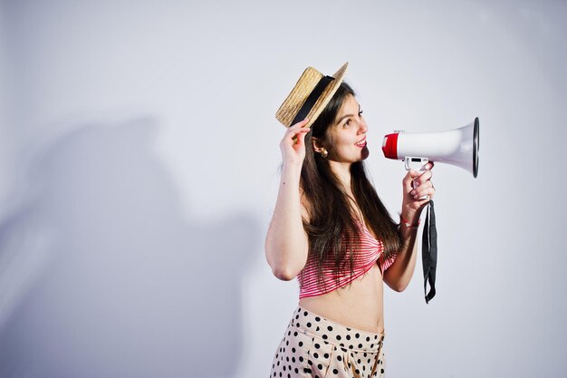 Portrait of a gorgeous young girl in swimming suit and hat talks into megaphone in studio