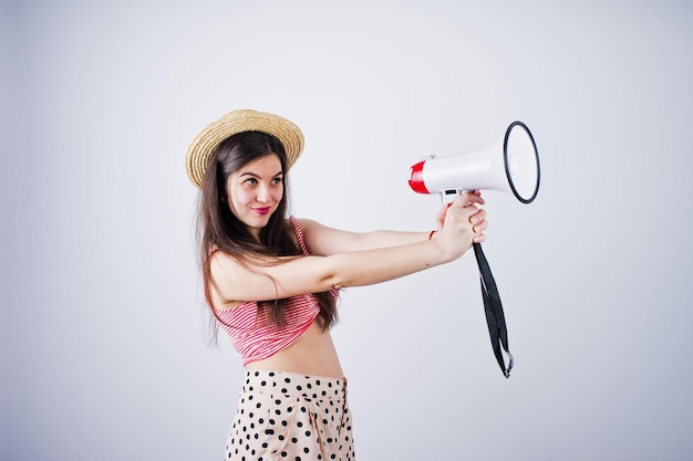 Ritratto di una splendida ragazza in costume da bagno e cappello parla nel megafono in studio