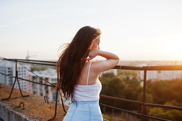 Free photo portrait of a gorgeous young woman in casual clothing admiring the sunset from the roof of a building