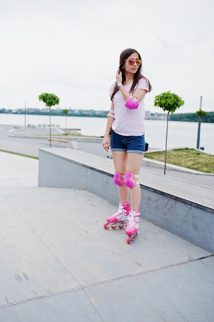 Portrait of a gorgeous young woman in shorts tshirt and sunglasses standing outdoor in rollerblades