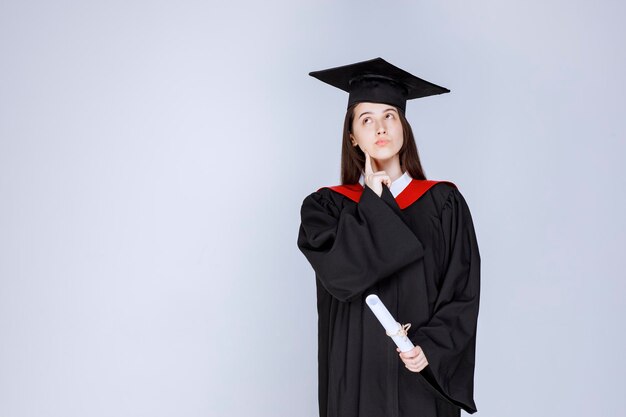 졸업장을 들고 서 있는 가운을 입은 대학원생의 초상화. 고품질 사진