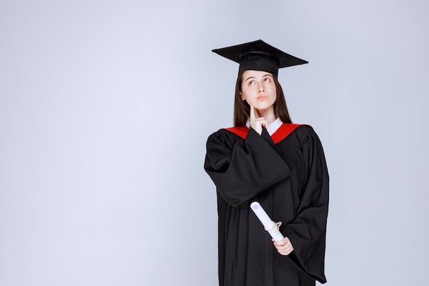 Portrait of graduate student in gown holding diploma and standing. High quality photo