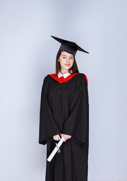 졸업장을 들고 서 있는 가운을 입은 대학원생의 초상화. 고품질 사진
