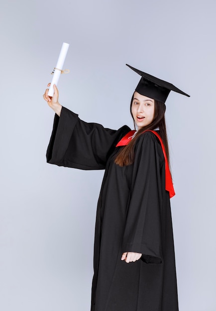 Portrait of graduate student in gown showing college certificate. High quality photo