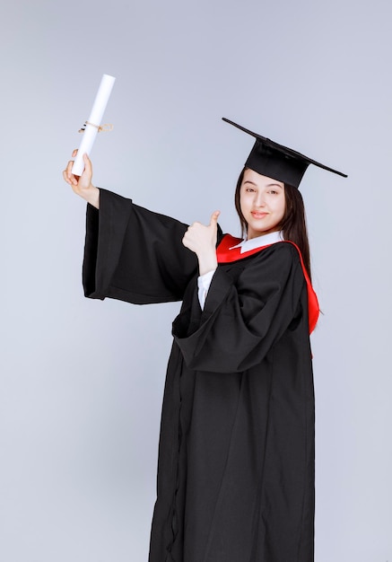 Portrait of graduate student in gown showing college certificate. High quality photo