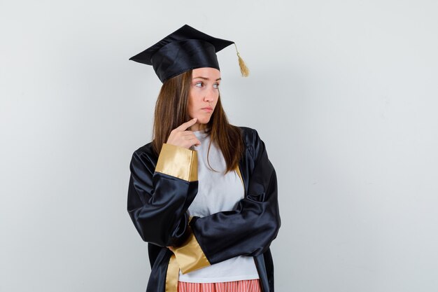 Portrait of graduate woman holding finger on chin in casual clothes, uniform and looking thoughtful front view