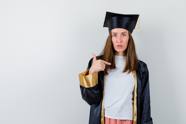 Портрет выпускницы, указывающей на себя в повседневной одежде, униформе и озадаченной, вид спереди