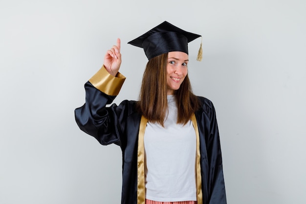Портрет выпускницы, указывая вверх в повседневной одежде, униформе и веселый вид спереди