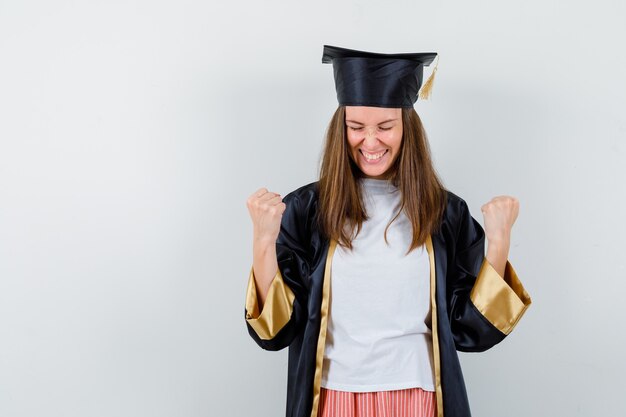 カジュアルな服装、制服、幸せな正面図で勝者のジェスチャーを示す大学院の女性の肖像画