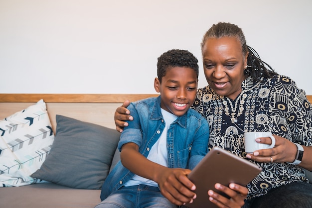 Portrait of grandmother and grandchild taking selfie with digital tablet while sitting on sofa couch at home. Family and lifestyle concept.