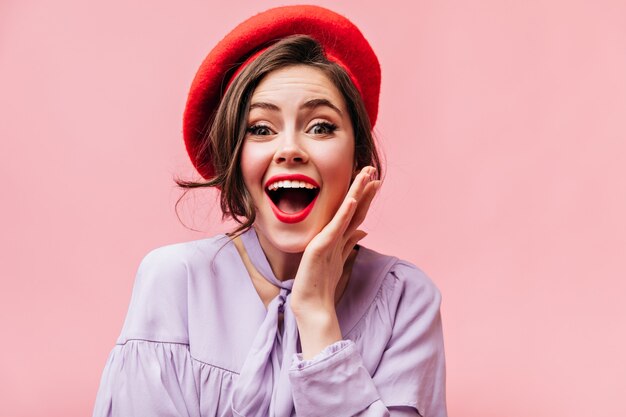 Portrait of green-eyed curly woman with red lipstick. Girl in red beret in joyful surprise looks into camera.