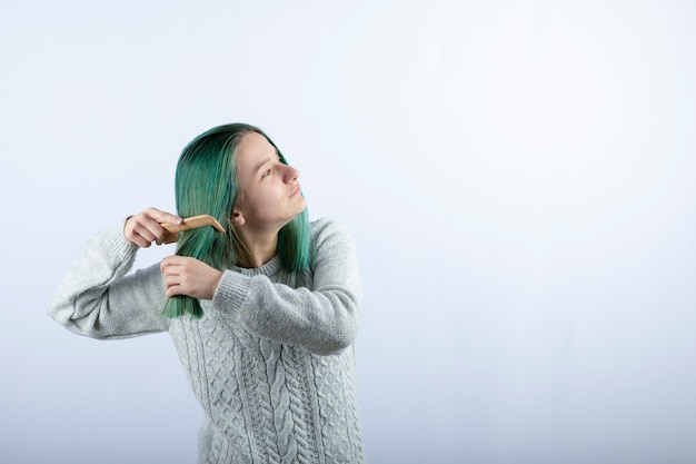 Ritratto di ragazza dai capelli verdi che pettina i suoi capelli sul grigio.