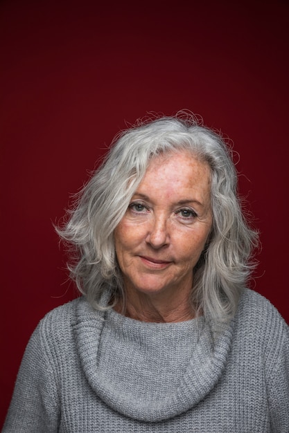 Portrait of a grey senior woman standing against red backdrop