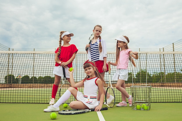 Free photo portrait of group of girls as tennis players holding tennis rackets against green grass of outdoor court.