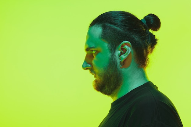 Portrait of a guy with colorful neon light on green studio background. Male model with calm and serious mood.