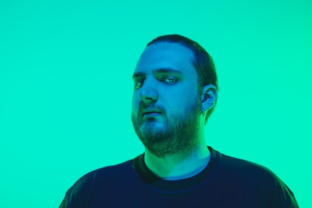 Portrait of a guy with colorful neon light on green  wall. Male model with calm and serious mood. Facial expression, millenials lifestyle and look like. Future, technologies.