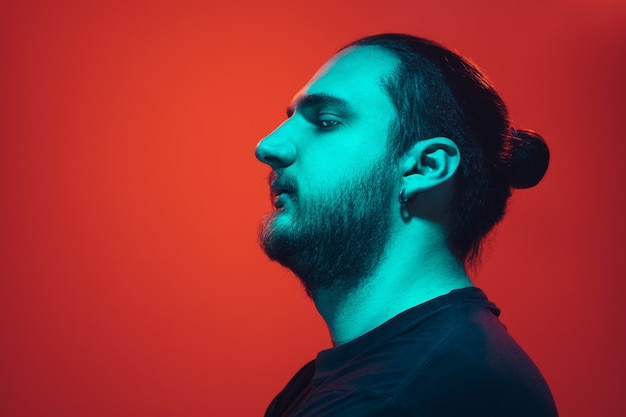 Portrait of a guy with colorful neon light on red studio background. Male model with calm and serious mood.