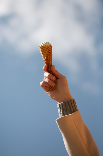 Free photo portrait of hand holding ice cream cone against sky