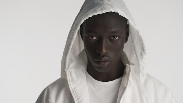 Portrait of handsome African American man dressed in white jacket with hood posing on camera with serious look isolated on white background