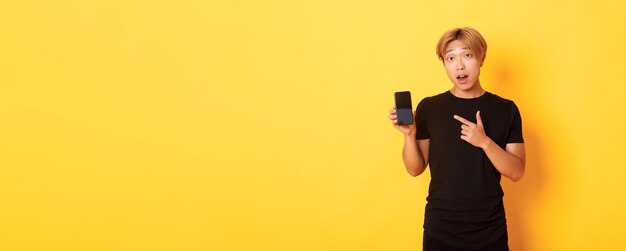 Portrait of handsome asian man showing something on smartphone screen pointing at mobile phone displ