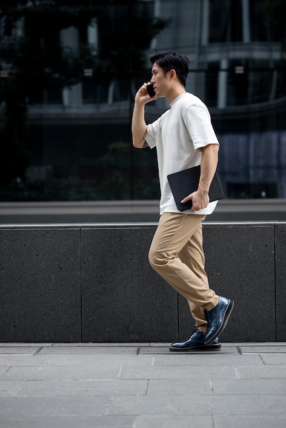 Foto gratuita ritratto di un bell'uomo asiatico che utilizza smartphone all'aperto in città