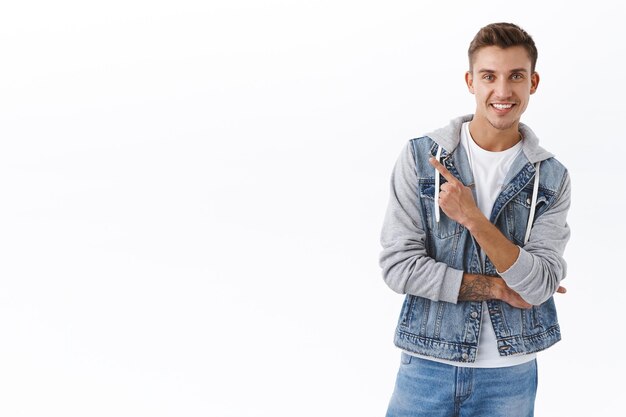 Portrait of handsome blond guy pointing finger upper left corner, smiling satisfied