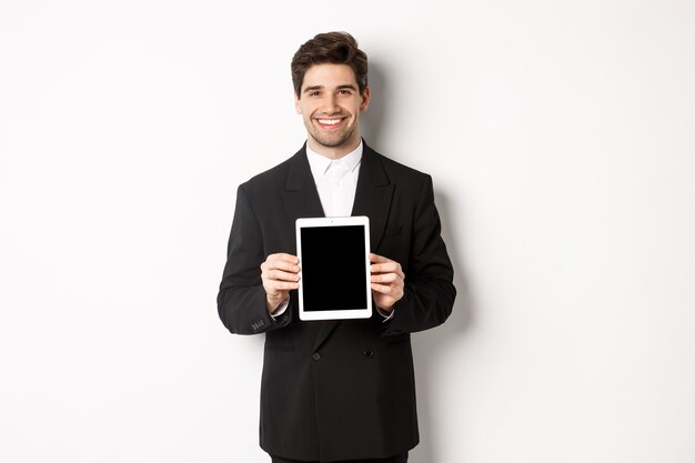 トレンディなスーツを着たハンサムなビジネスマンの肖像画、デジタルタブレット画面を表示し、笑顔、白い背景に立って