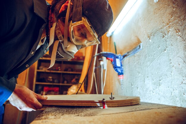 Portrait of handsome carpenter working with wooden skate at workshop, profile view