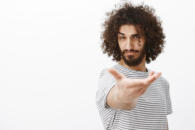 Portrait of handsome confident macho man with beard and curly hair, pulling hand towards