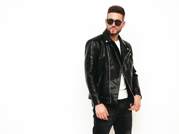 Portrait of handsome confident model Sexy stylish man dressed in biker leather jacket and black jeans Fashion hipster male isolated on white in studio In sunglasses